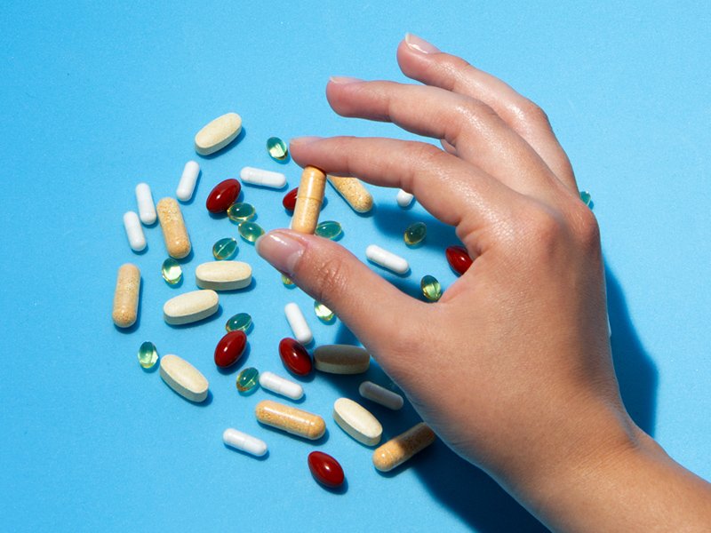 Life Extensio, supplements on a blue background and hand picking an orange capsule with two fingers